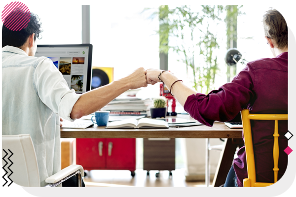 Two guys fist bumping each other while sitting at a desk