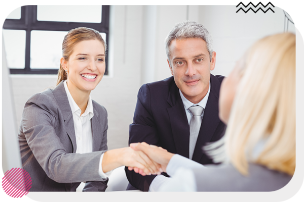 Woman and man sitting next to each other while the woman shakes hands with someone across the table