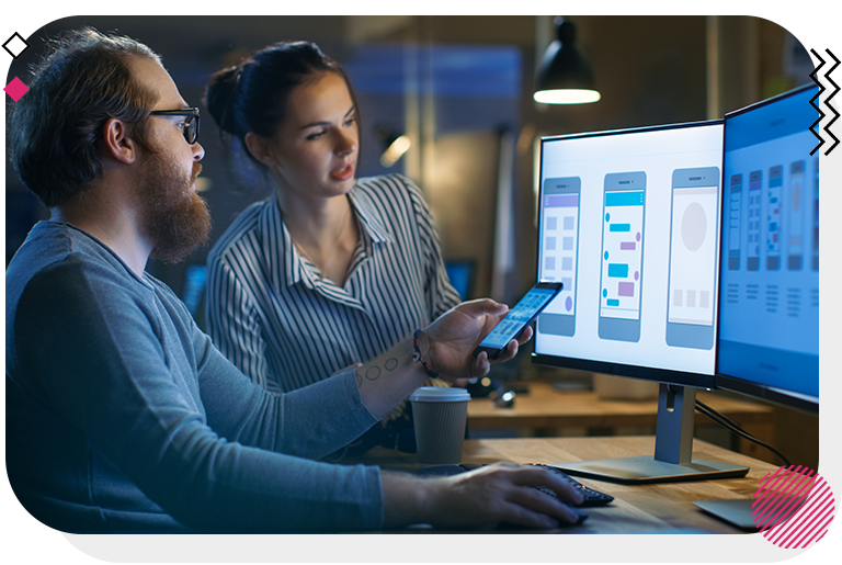 Man and woman looking at prototypes on cell phone and 2 monitors