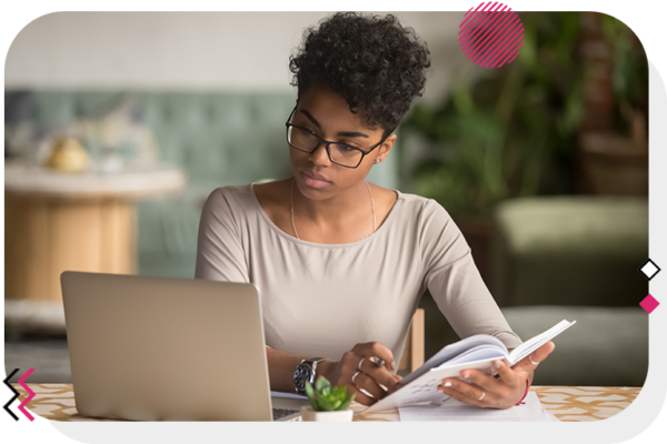 Woman sitting at desk looking at computer screen and flipping through notebook