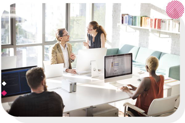 A desk with 2 people on their computer and 2 people talking on the other side