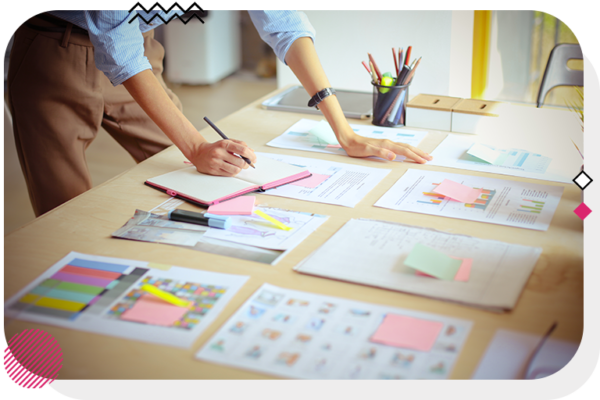 Person writing a note on a desk covered in papers and sticky notes