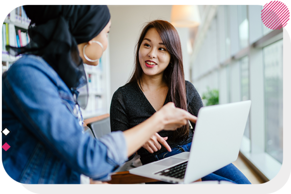 Two women talking while one holds her laptop to show the other woman